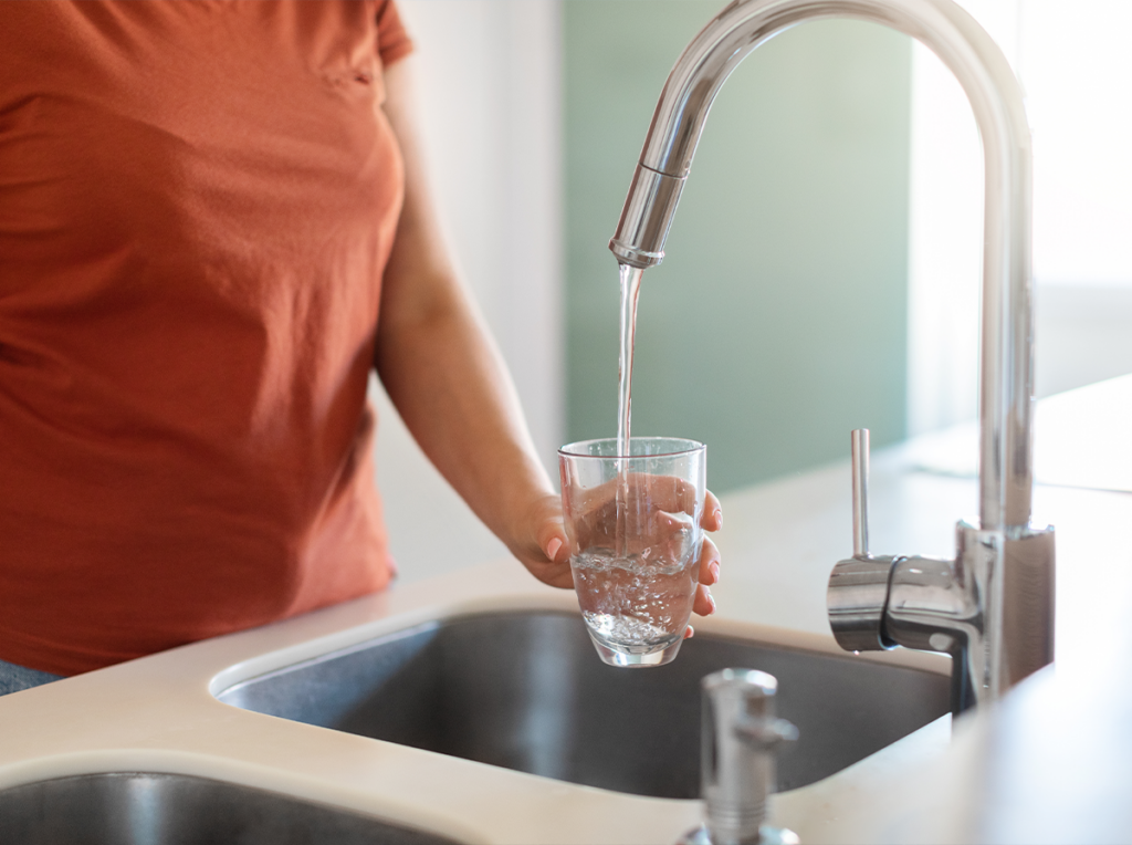 Person filling a glass with tap water at a kitchen sink, representing everyday changes in water taste and feel.